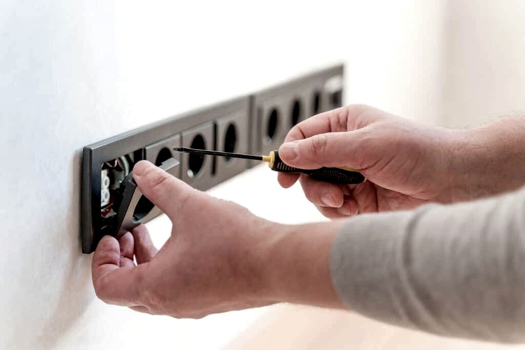 Electrician installs sockets in the wall of a new apartment